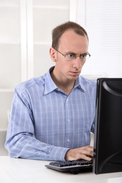 Glatzköpfiger Geschäftsmann im blauen Hemd arbeitet im Büro am Computer. — Stockfoto