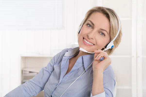 Tevreden volwassen zakenvrouw met hoofdtelefoon op kantoor. Stockfoto