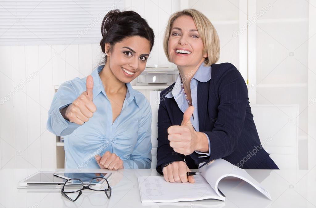 Two successful business women with thumbs up at office.