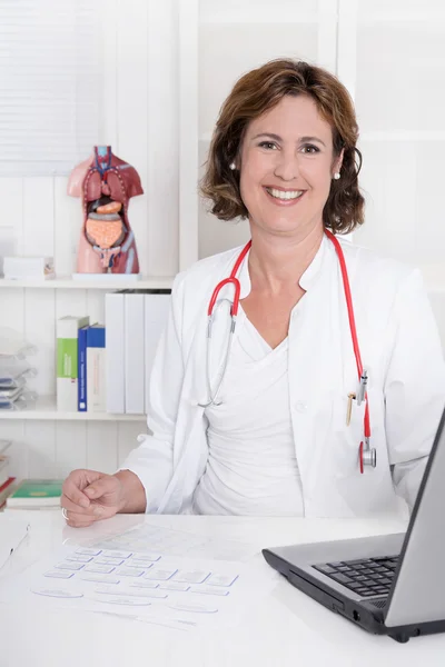 Porträtt av ganska brunett leende läkare arbetar på skrivbordet. — Stockfoto