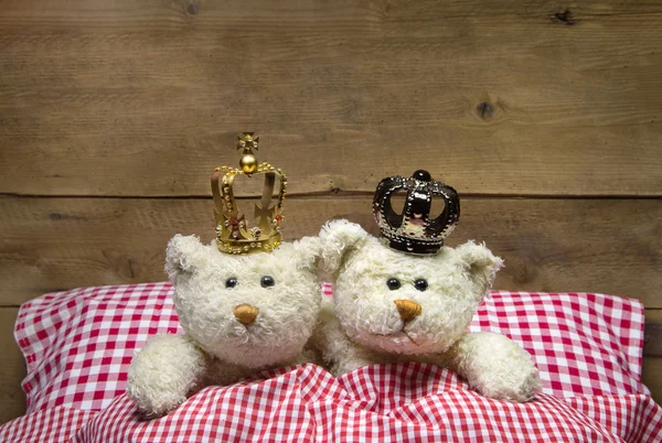 Dos osos de peluche beige tumbados en una cama a cuadros con coronas . —  Fotos de Stock