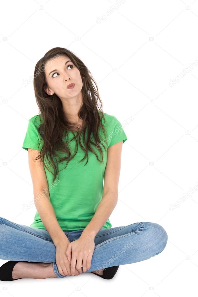 Isolated young pensive woman sitting with crossed legs.