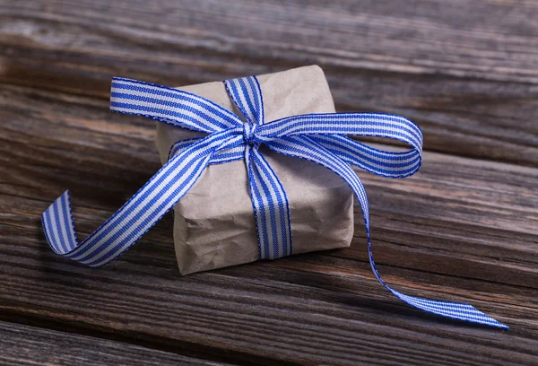 Gift box wrapped in natural paper with blue ribbon. — Stock Photo, Image