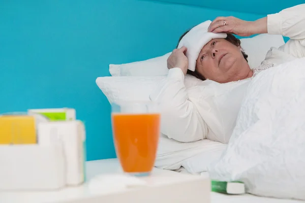 Senior woman laid ill in the bed with medicament and pillows, — Stock Photo, Image