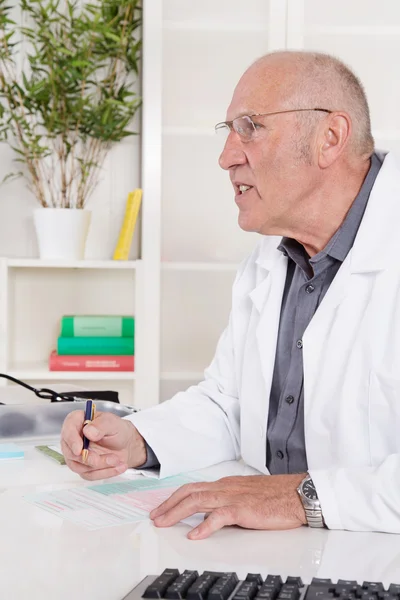 Retrato de un médico mayor sentado en el escritorio . — Foto de Stock