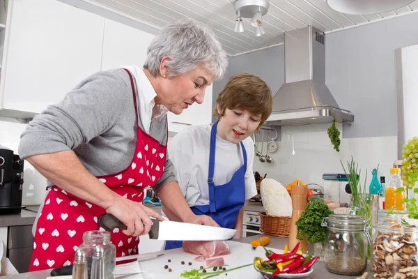 Mormor med barnbarn i köket förbereder stekt kött. — Stockfoto