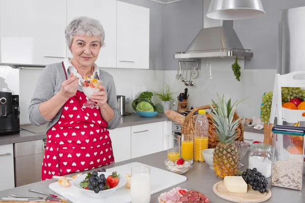 Oudere gelukkig vrouw eten yoghurt in de ochtend. — Stockfoto
