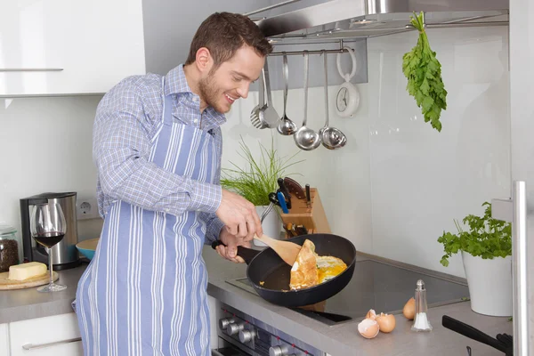 Ung man i köket matlagning stekt ägg. — Stockfoto