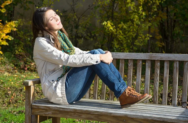 Jonge vrouw zittend op een park bench en geniet van het najaar. — Stockfoto