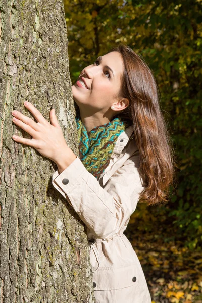 Glückliche junge Frau im Herbst, die einen Baum umarmt. — Stockfoto