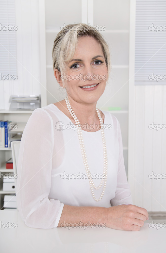 Successful attractive blond older businesswoman sitting at desk.