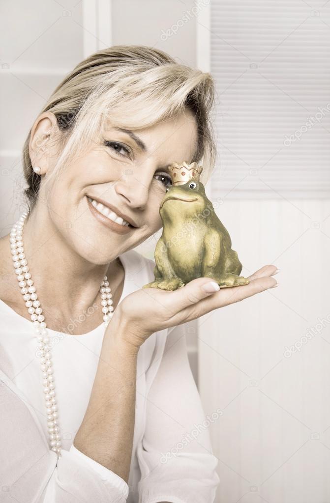 Pretty smiling older woman with a green frog in her hands. Conce