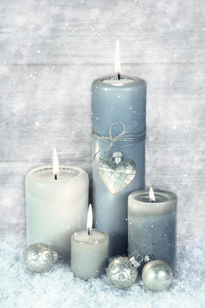 Four blue, grey and white burning christmas candles with snow in