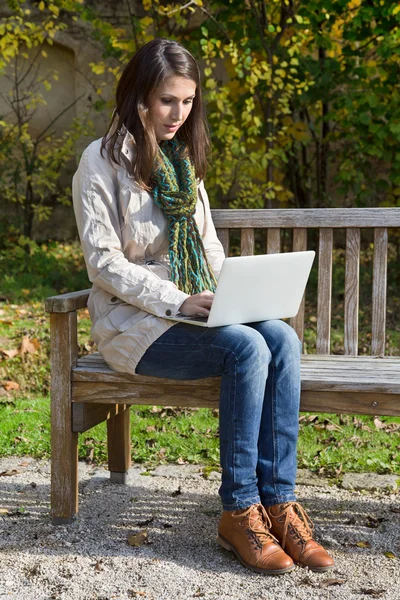 Mujer joven en otoño sentada en un banco del parque escribiendo algo — Foto de Stock