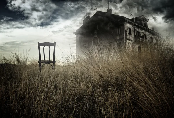 Abandoned chair out in a field facing a haunted house Stock Photo