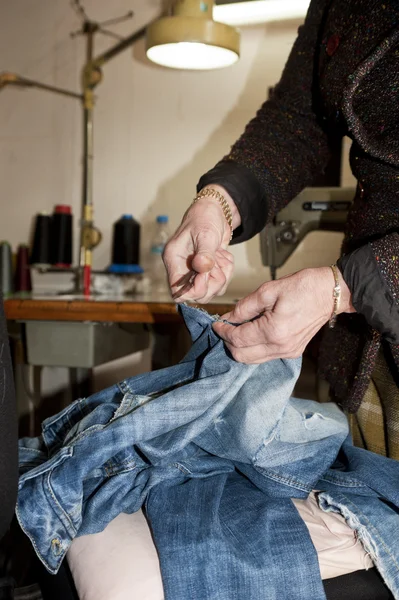 Tailor repairing a pair of old jeans in her workshop — Stock Photo, Image