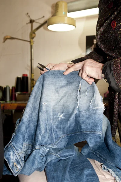 Tailor repairing a pair of old jeans in her workshop — Stock Photo, Image