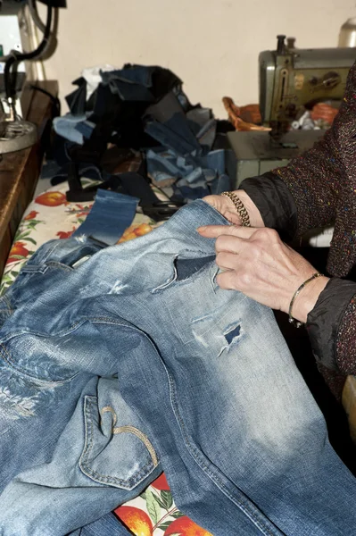 Tailor repairing a pair of old jeans in her workshop — Stock Photo, Image