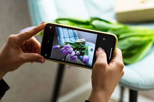 Mor lale çiçeklerinin fotoğrafıyla, kadınların elleri telefonu tutuyor.