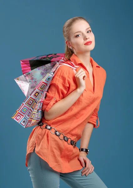 Girl in an orange shirt and jeans with shopping bags — Stock Photo, Image