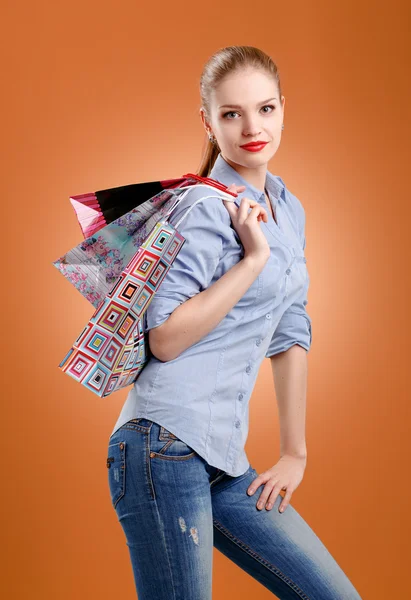 Girl in an orange shirt and jeans with shopping bags — Stock Photo, Image