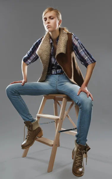 Androgynous girl sits on a chair. Jeans and jacket. — Stock Photo, Image