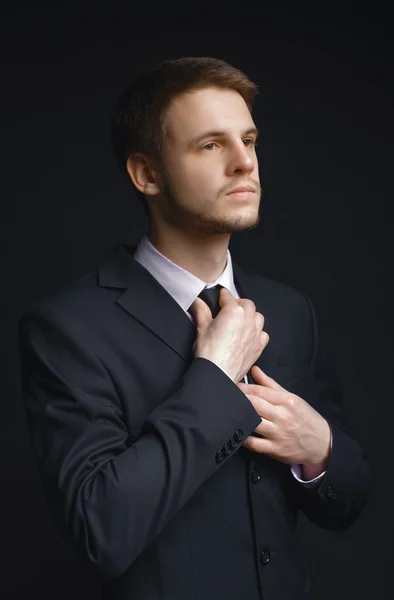 Young businessman in elegant suit straightens his tie. — Stock Photo, Image