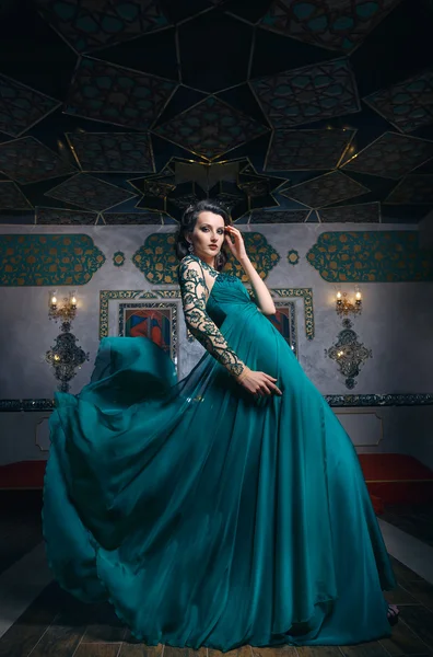 Mulher bonita em um vestido longo verde em um fundo de ricamente — Fotografia de Stock