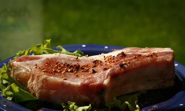 Bife de porco cru polvilhado com pimenta na placa azul com salada — Fotografia de Stock