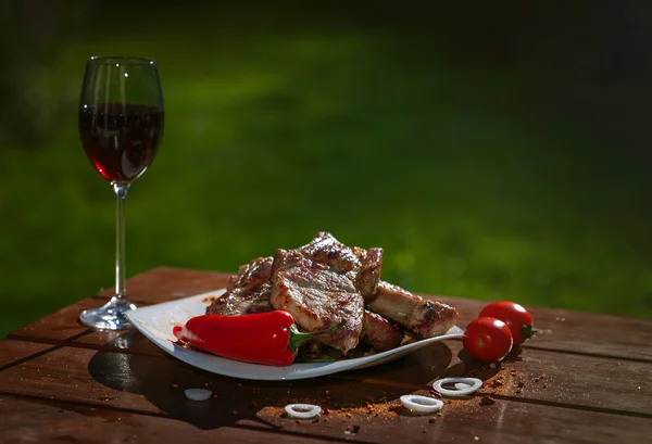 Grilled pork steaks on a wooden table with a glass of wine