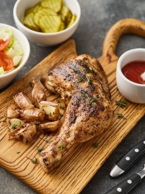 Grilled chicken leg with garlic and pickles on a wooden board.