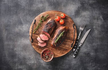 Roasted duck breast on a round wooden board with peppers and cherry tomatoes