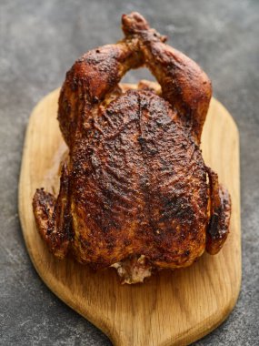 Whole barbecue chicken on a wooden board on a gray background.
