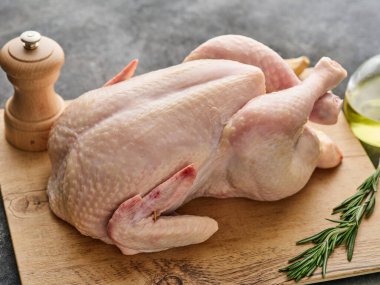 Whole raw chicken on a wooden board on a gray background. Raw chicken with spices