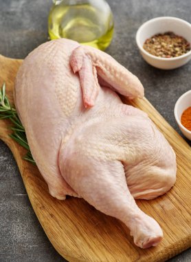 Fresh half of raw chicken with spices and seasonings on a wooden board