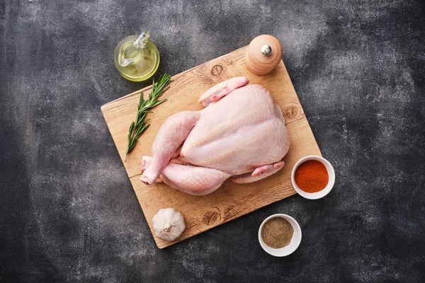 Whole raw chicken on wooden board on dark background. Preparing raw chicken. Top view.