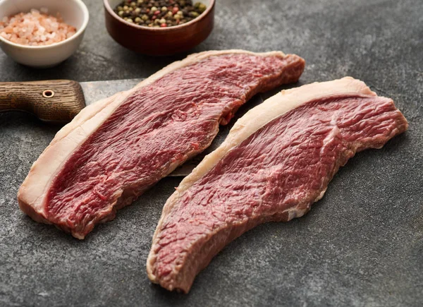 Raw cap rump steak or top sirloin beef meat steak on grey table. Grey background.