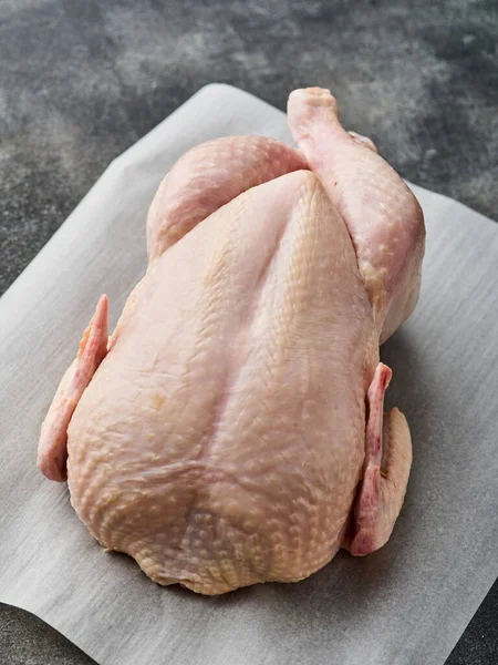 A whole raw chicken is placed on white paper. Preparing raw chicken.