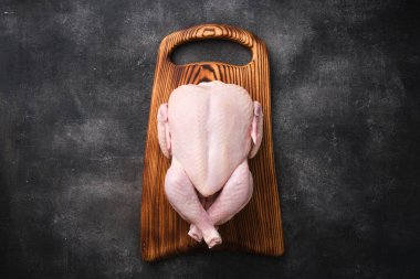 Whole raw chicken on wooden board on dark background. Preparing raw chicken. Top view.