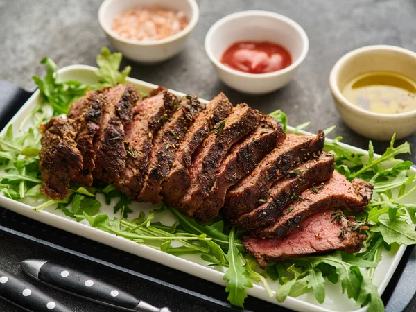 Beef tenderloin steak. Grilled sliced beef steak on white plate over grey table. Filet Mignon recipe