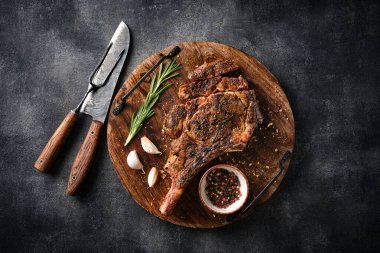 Tahta kesme tahtasında taze ızgara Tomahawk bifteği, mangal yemeği, üst manzara, gri arka plan.