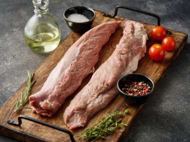 Gri arka planda çiğ domuz filetosu, yakın plan. Tahtada pişmeye hazır taze çiğ domuz filetosu.