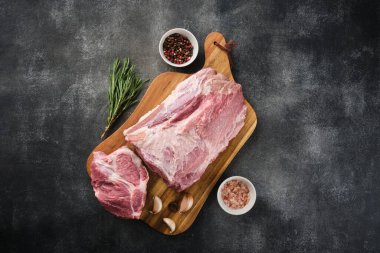 Çiğ domuz boyunlu et, sebze yaprakları ve ahşap tahtada baharatlar. Gri arka plan. Üst görünüm