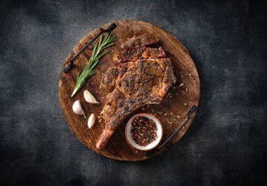 Tahta kesme tahtasında taze ızgara Tomahawk bifteği, mangal yemeği, üst manzara, gri arka plan.