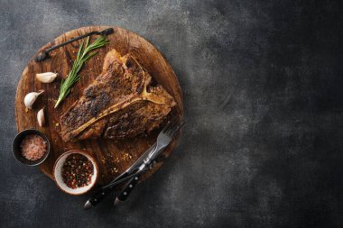 Koyu gri arka planda kesilmiş tahtada tuzlu ve biberli ızgara T-Bone bifteği. Kızarmış T-Bone bifteği.
