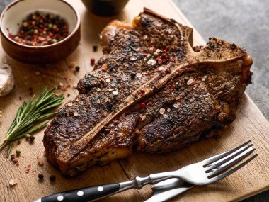 Koyu gri arka planda kesilmiş tahtada tuzlu ve biberli ızgara T-Bone bifteği. Kızarmış T-Bone bifteği.