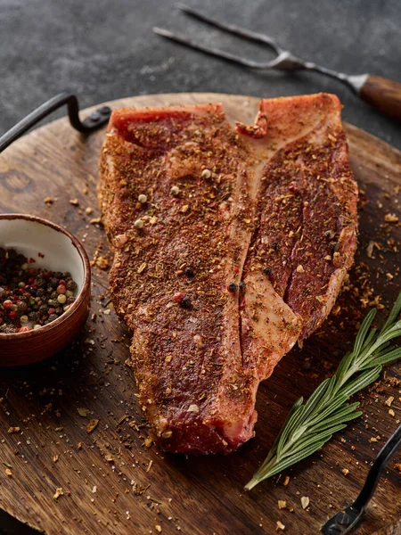 生の新鮮な肉のTボーンステーキ 灰色の背景に木の板を切る調味料 — ストック写真