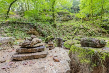 Bir kaya formasyonunda Cairns veya Apachitas, toprak patika, yosun, ağaçlar ve arka planda yeşil yabani bitki örtüsü, yaz günü Mullerthal Trail yürüyüş rotasında, Lüksemburg