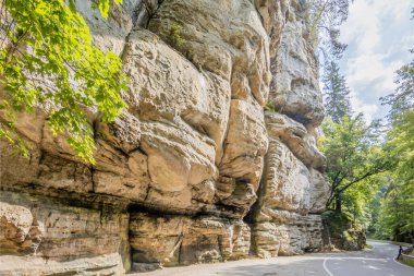 Yüzeyinde aşınma ve oyuklar olan engebeli kayalık dağlar, arka planda yeşil ağaçlar, Lüksemburg 'daki Mullerthal Trail' de doğa yürüyüşü için sakin bir yaz günü.