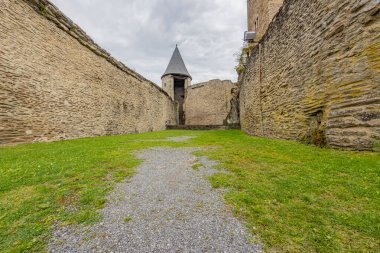 Zemindeki yeşil çimenler, arka plandaki bozulmuş taş duvarlar, gözetleme kulesi, ortaçağ Bourscheid kalesi, bulutlu bir gün, gri bulutlarla kaplı bir gökyüzü, Lüksemburg